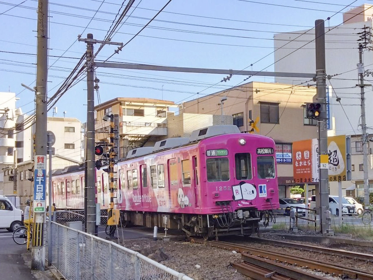 高松市街の踏切付近を通過する楽天モバイル車両の後方。長尾線の走行シーン